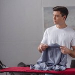 Hombre guapo sosteniendo camisa para planchar en la sala de estar y mirando hacia otro lado