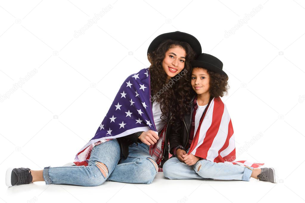 mother and daughter covered in usa flag sitting on floor isolated on white