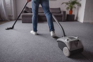 oturma odasında elektrikli süpürge ile halı yıkama adamın Resim kırpılmış