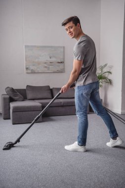 Elektrikli süpürge ile halı yıkama ve kamera oturma odasında bakarak yakışıklı adam