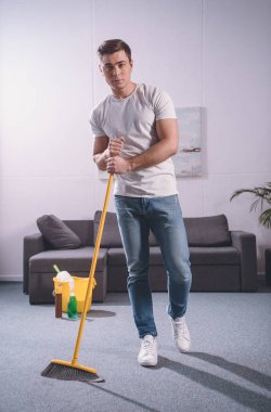 oturma odası süpürge ile süpürme ve kameraya bakarak yakışıklı adam