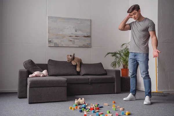 Mann Steht Und Sieht Auf Dem Boden Verstreutes Kinderspielzeug — Stockfoto