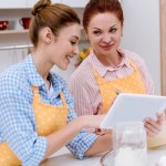 Mujer joven y su madre usando tableta juntos en la cocina mientras cocinan