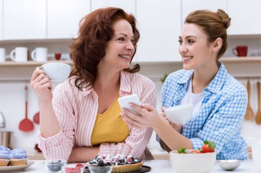 mutlu genç kadın ve annesi tatlılar ile kahve içme ve smartphone birlikte kullanma