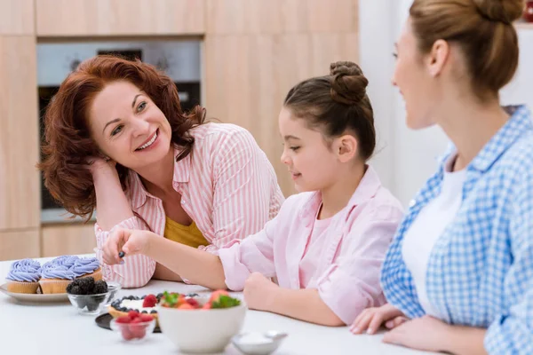 世代の女性の果実とデザートを一緒に飾るとキッチンで話して — ストック写真