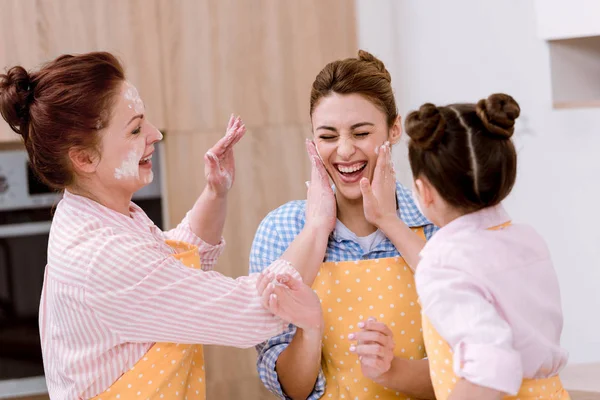 キッチンで小麦粉と遊ぶ女性を笑いの三世代 — ストック写真