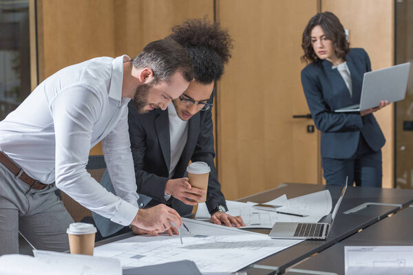 команда архитекторов, работающих с планами строительства в конференц-зале офиса
