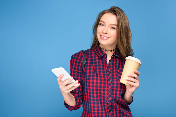 beautiful smiling girl with coffee using smartphone, isolated on blue