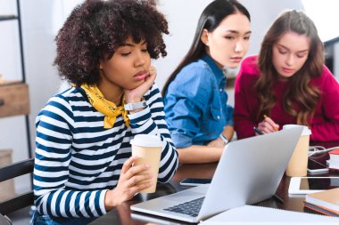 selective focus of bored african american young woman with laptop and multicultural students near by