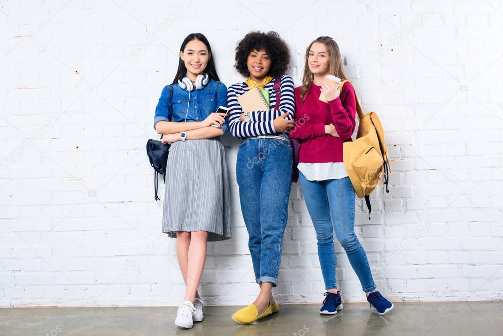 smiling multiracial students standing against white brick wall