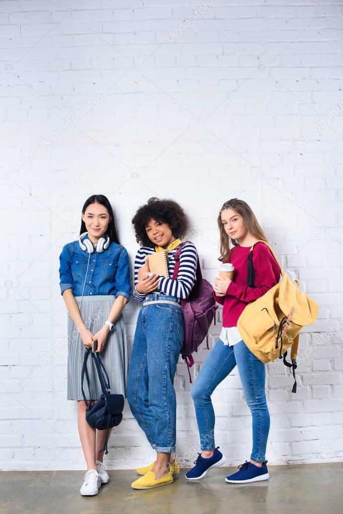 young multiracial students standing against white brick wall