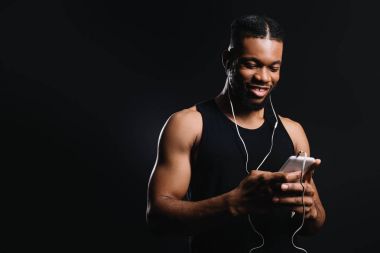 siyah izole smartphone kullanarak kulaklık gülümseyen kas Afrikalı-Amerikalı adam