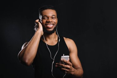 Afro-Amerikan erkekte kas smartphone kullanarak ve üzerinde siyah izole kamera gülümseyen kulaklık