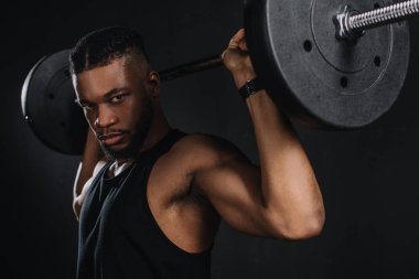 Halter kaldırma ve siyahta kameraya bakarak kas genç Afro-Amerikan sporcu
