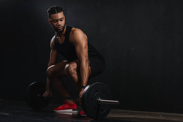 full length view of young african american sportsman lifting barbell on black 