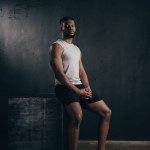 Vista completa de joven atlético afroamericano hombre en ropa deportiva sentado y mirando a la cámara en negro