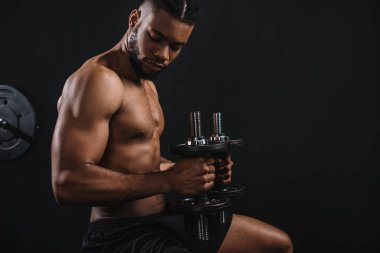 side view of muscular shirtless young african american man exercising with dumbbells on black clipart