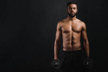 muscular shirtless african american man holding dumbbells and looking at camera isolated on black clipart