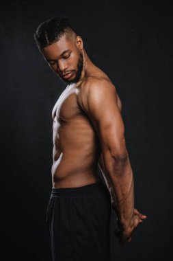 side view of shirtless muscular young african american man stretching hands isolated on black  clipart