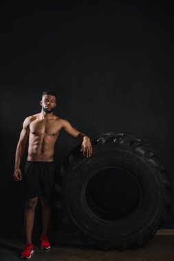 Lastik yaslanmış ve siyahta kameraya bakarak kas gömleksiz genç Afro-Amerikan sporcu