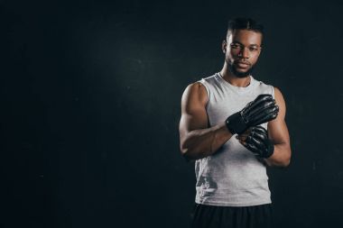 young african american kickboxer wearing gloves and looking at camera isolated on black clipart