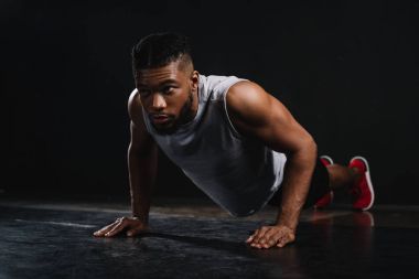 young muscular african american man in sportswear doing push-ups and looking away on black clipart