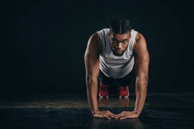 Genç Afro-Amerikan sporcu yapıyor tahta pozisyonu ve siyahta kameraya bakıyor