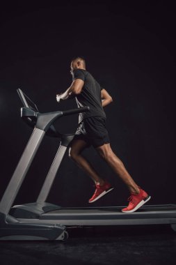 low angle view of young african american sportsman running on treadmill on black  clipart