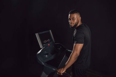 koşu bandında egzersiz ve siyahta izole kamera bakarak genç Afro-Amerikan sporcu