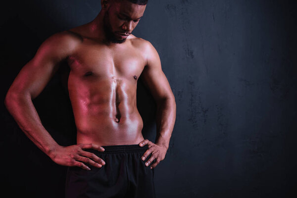 Мускулистый африканский американец с голыми грудями стоит с руками на талии и смотрит вниз на черный

