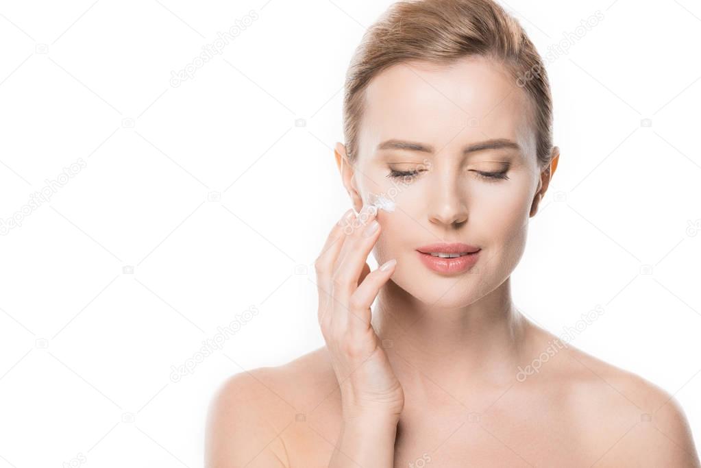 Female with closed eyes applying cream on her face isolated on white