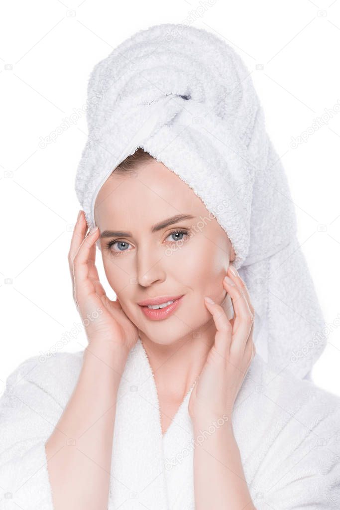Portrait of woman with clean skin in bathrobe and towel on hair touching own face isolated on white