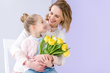 Cute child embracing mother with tulips bouquet on 8 march clipart