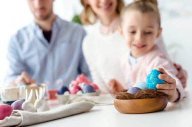 Child putting Easter egg in nest by her family clipart