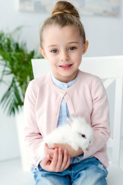 Beyaz tavşan kız çocuk dizlerinin üstüne oturuyor