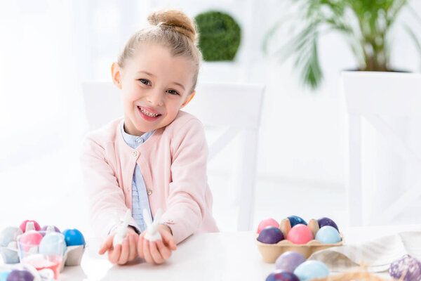Kid girl showing bunny statuettes by Easter eggs