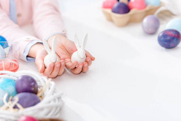 Close-up view of child showing bunny statuettes by Easter eggs