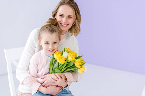 Hugging mother and daughter holding tulips for women's day