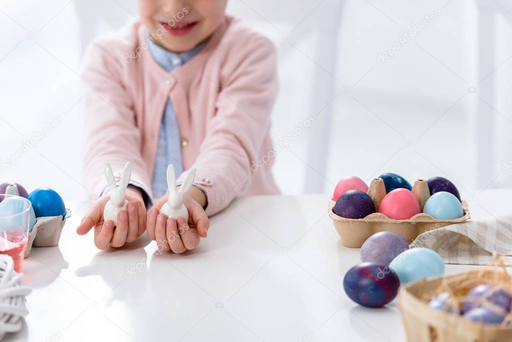 Close-up view of child on Easter holding bunny statuettes by painted eggs