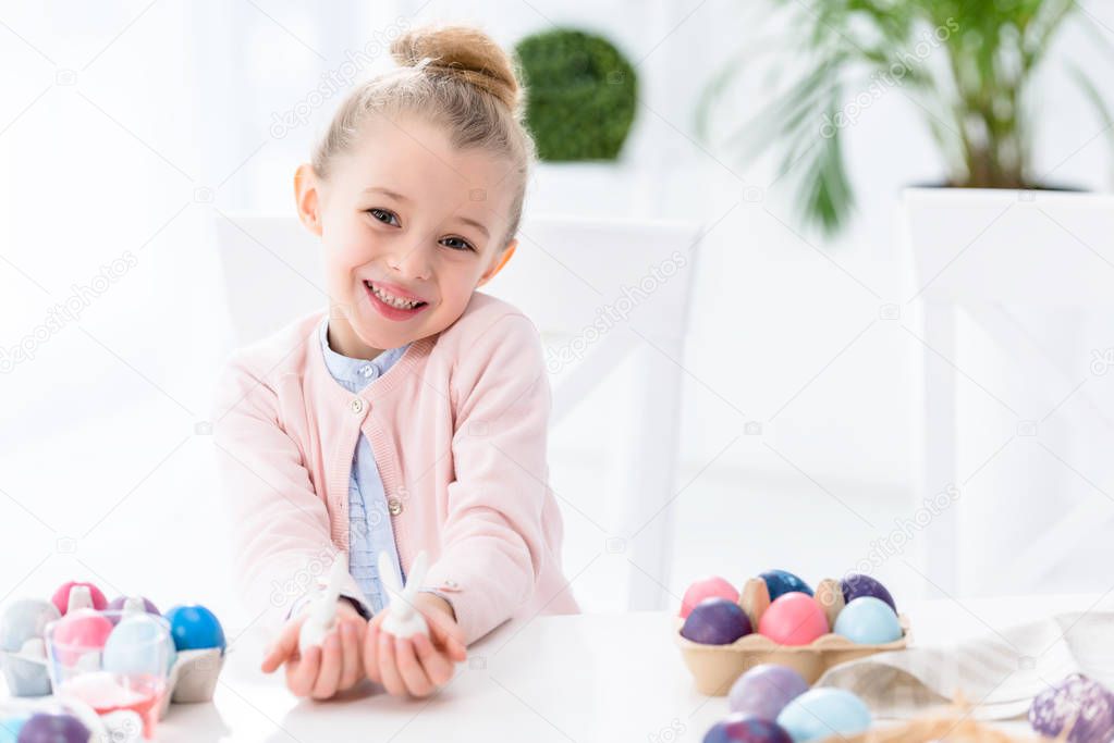 Kid girl showing bunny statuettes by Easter eggs