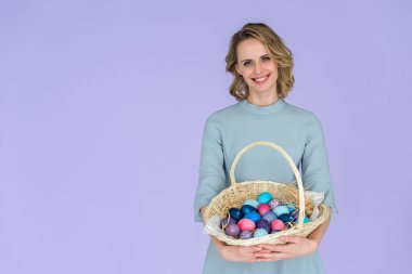 Violet izole Paskalya için renkli yumurta sepetle tutan çekici genç kadın