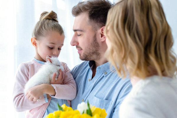 Очаровательная семья с дочерью, обнимающей кролика
