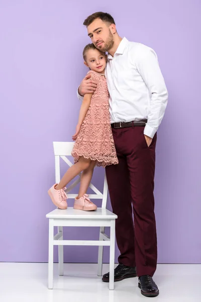 Vater Umarmt Kleine Tochter Auf Stuhl Auf Violettem Hintergrund — Stockfoto