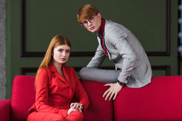 Couple of young fashion model dressed in suits on couch