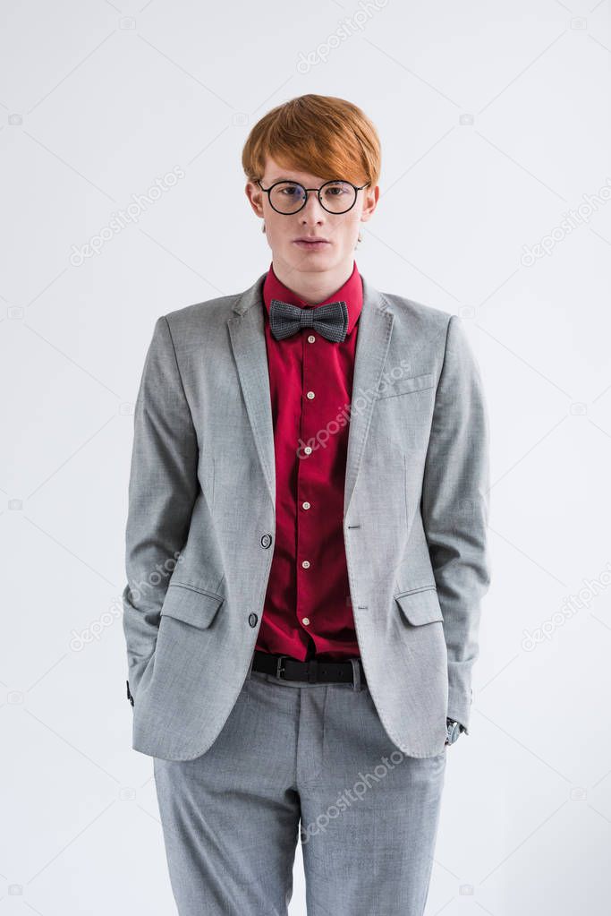Young male fashion model in eyeglasses with hands in pockets isolated on grey