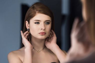 Young stylish female model with earrings looking at own reflection