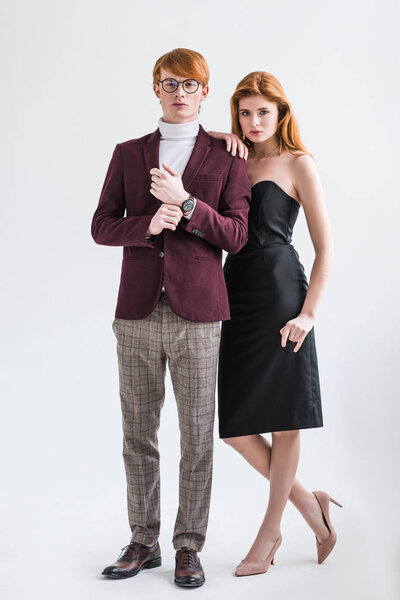 Male fashion model adjusting wristwatch while young female standing beside isolated on grey