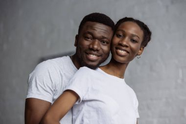 happy young african american couple in white t-shirts smiling at camera clipart