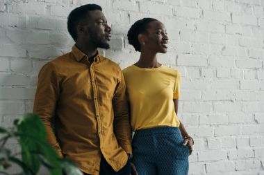 güzel şık genç Afro-Amerikan çift ayakta beyaz duvara yakın ve uzak arıyorsunuz