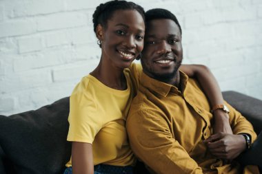 mutlu genç Afro-Amerikan kaç sarılma ve kameraya gülümseyen sarı gömlek içinde